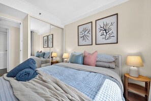 A bedroom with a bed, bedside lamps, a mirror, and wall art. - Wellington Breeze – Mosman Park – 2BR with Pool & Balcony (Mosman Park)