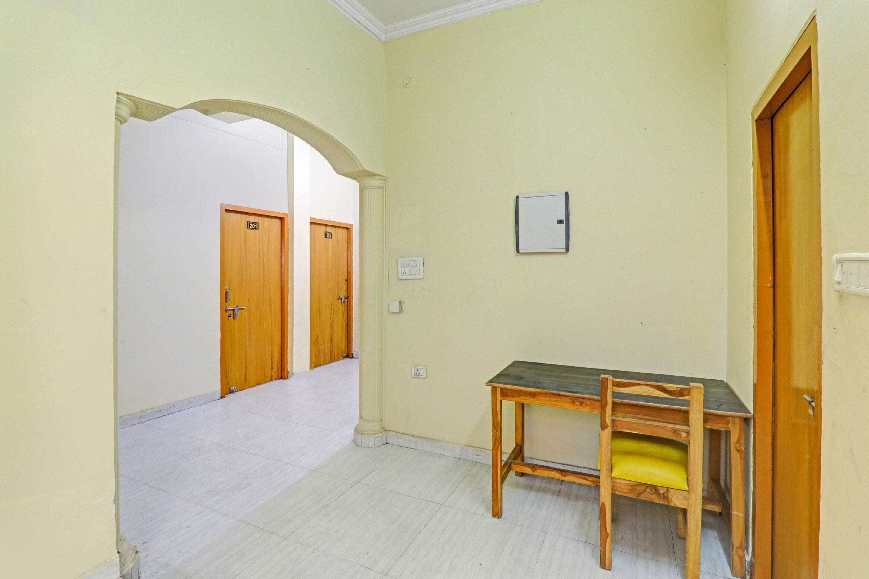 A hallway with two wooden doors, a small table with a cushion, and a light switch on the wall.