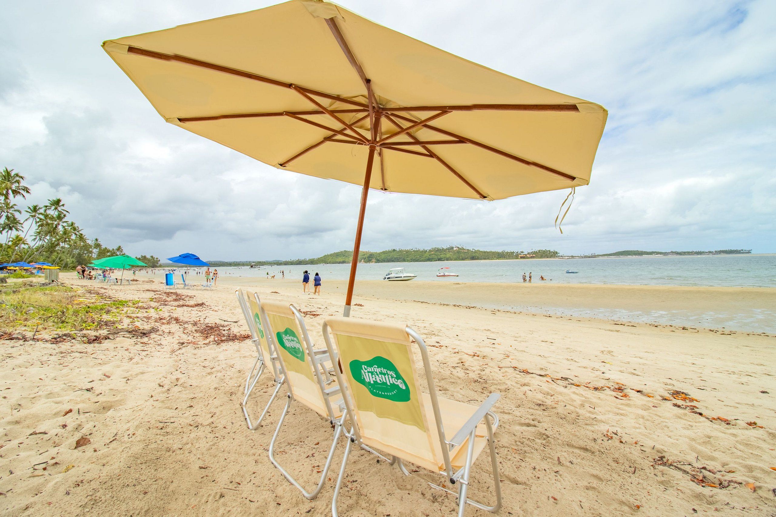 Beach chairs with a logo, a large umbrella, and a view of the beach and water.