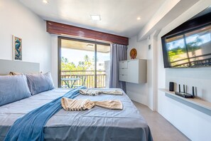 A modern bedroom with a bed, a TV, a balcony, and a view of palm trees. - Carneiros Atlantico #4222 Beachfront by Carpediem (Tamandaré)