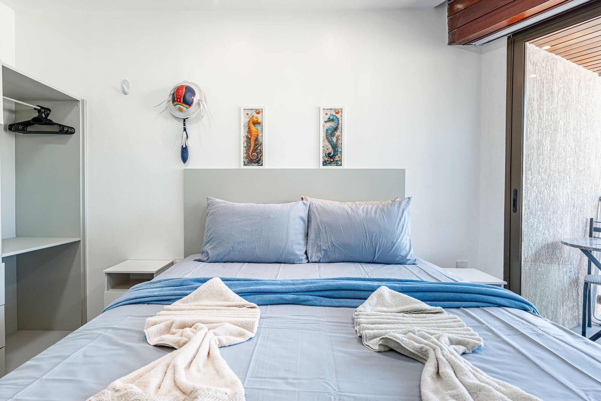 Un dormitorio con una cama, almohadas, una toalla, un sombrero colgado y dos cuadros en la pared.