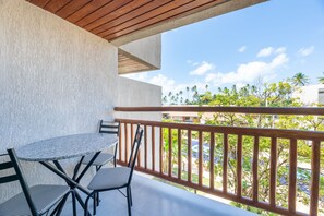 A balcony with a table and chairs, overlooking a pool and palm trees. - Carneiros Atlantico #4222 Beachfront by Carpediem (Tamandaré)
