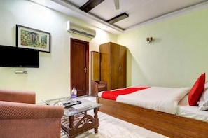 Una habitación de hotel con una cama, una mesa de centro de vidrio, una silla, un armario y un televisor.