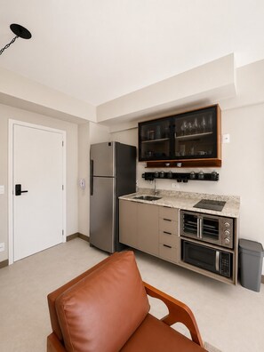 A compact kitchen with a refrigerator, oven, microwave, and a built-in oven range. There is a cabinet with glass doors above the countertop. - SETIN 1006 (São Paulo)