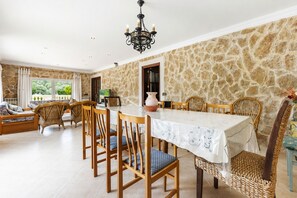 A dining area with a stone wall, a chandelier, wicker furniture, and a view of greenery outside. - Vistabona, 5StarsHome Mallorca Villa (Capdepera)