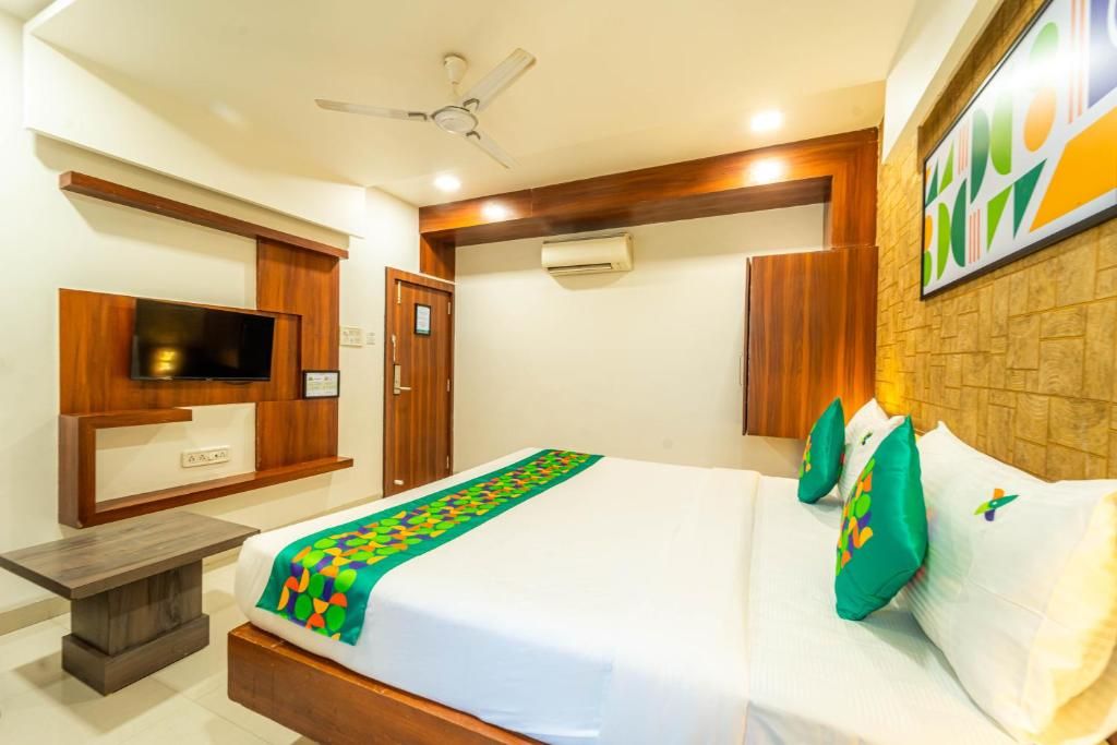 A hotel room with a bed, a television, a ceiling fan, and a wall-mounted air conditioning unit.