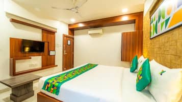 A hotel room with a bed, a television, a ceiling fan, and a wall-mounted air conditioning unit.