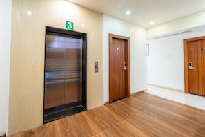 A hallway with an elevator marked with the number 3, wooden doors, and a tiled floor. - Treebo Ten Eleven Grand, Scheme 78 (Indore)