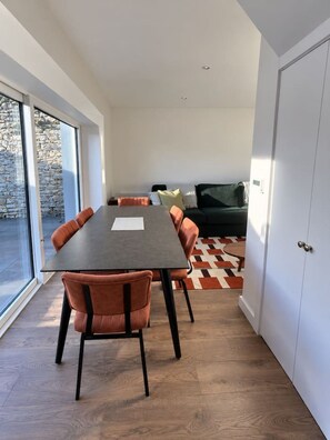 A modern interior with a dining table, chairs, a sofa, and a large window. - The Coach House

1 Chapel Lane (Killarney)