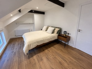 A bedroom with a sloped ceiling, a bed, a bedside table with a lamp, and a radiator. - The Coach House

1 Chapel Lane (Killarney)