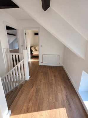 A hallway with wooden flooring, white walls, and a white radiator. A staircase with white railings leads to another room. - The Coach House

1 Chapel Lane (Killarney)