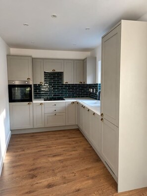 A kitchen with white cabinets, a black microwave, and a backsplash with dark tiles. - The Coach House

1 Chapel Lane (Killarney)