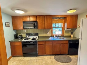 A kitchen with wooden cabinets, a microwave, stove, sink, and dishwasher. - Relax and enjoy all that the Cape has to offer in this 3 bedroom home. (Dennis Port)