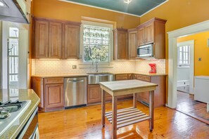 A kitchen with wooden cabinets, a stainless steel refrigerator, and a window with curtains.