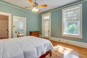 A bedroom with a bed, a dresser, a ceiling fan, and large windows.