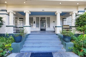 A building entrance with a set of stairs leading up to a door, flanked by columns and potted plants.