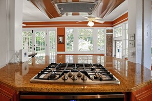 A kitchen with a gas stove, large windows, and a ceiling fan.