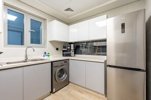 Une cuisine moderne avec des meubles blancs, un réfrigérateur en acier inoxydable, un lave-vaisselle et une fenêtre donnant sur un paysage bleu.
