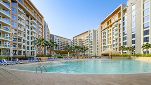 A modern hotel with a central swimming pool surrounded by lounge chairs and palm trees. - Majestic Hajar Mountain Views 1BR and Beach Access, Near Khorfakkan Amphitheatre (Khor Fakkan)