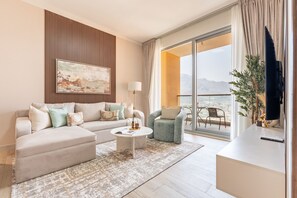 A modern living room with a sofa, armchair, coffee table, and a large window with a view. - Majestic Hajar Mountain Views 1BR and Beach Access, Near Khorfakkan Amphitheatre (Khor Fakkan)