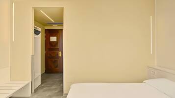 A hotel room with a bed, a desk, a wardrobe, and a door leading to another room.