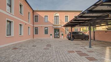 A courtyard with a paved ground, a building with multiple windows, and a parked car.