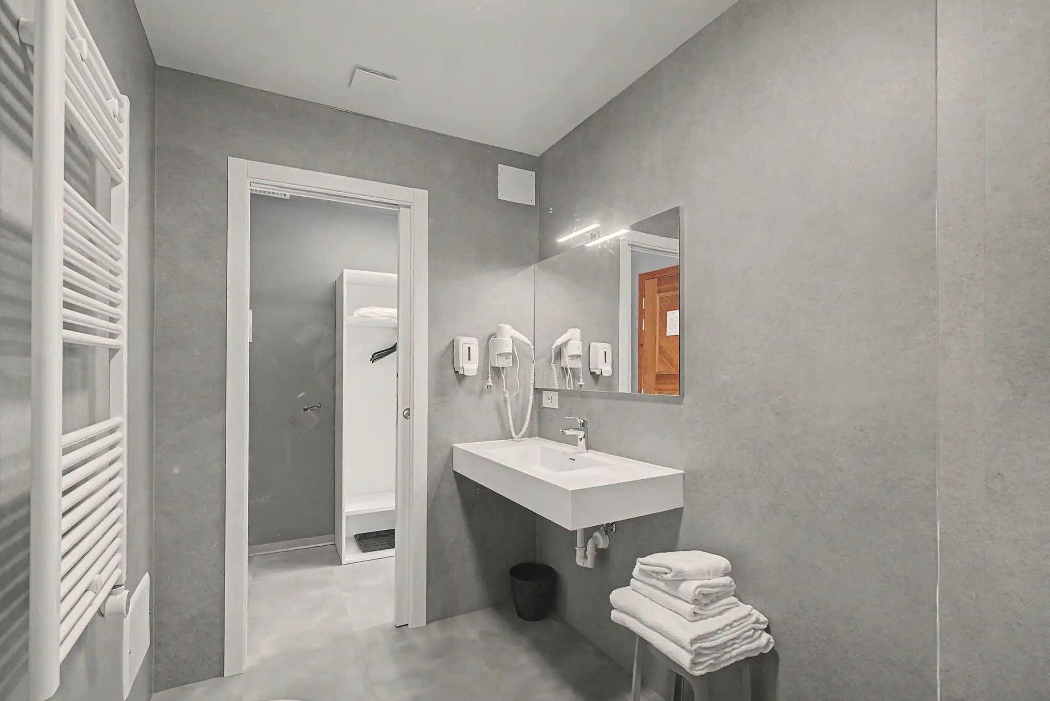A modern bathroom with a white sink, a mirror, and a towel stack.