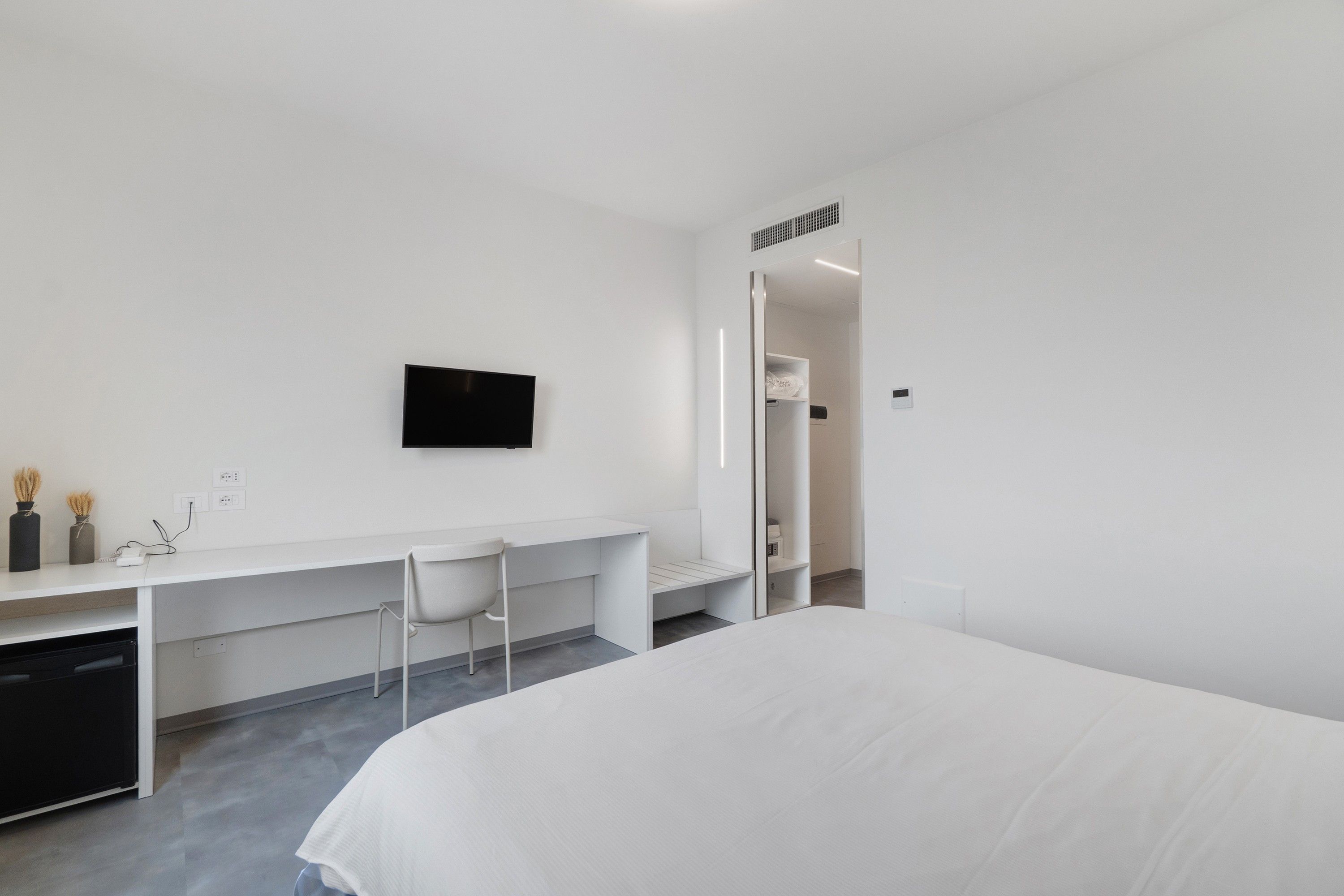 Ein modernes Hotelzimmer mit Bett, Schreibtisch, Stuhl, Fernseher und Kleiderschrank.