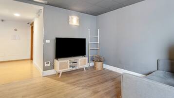 A room with a flat-screen TV on a wooden stand, a white ladder, and a woven basket with dried flowers.
