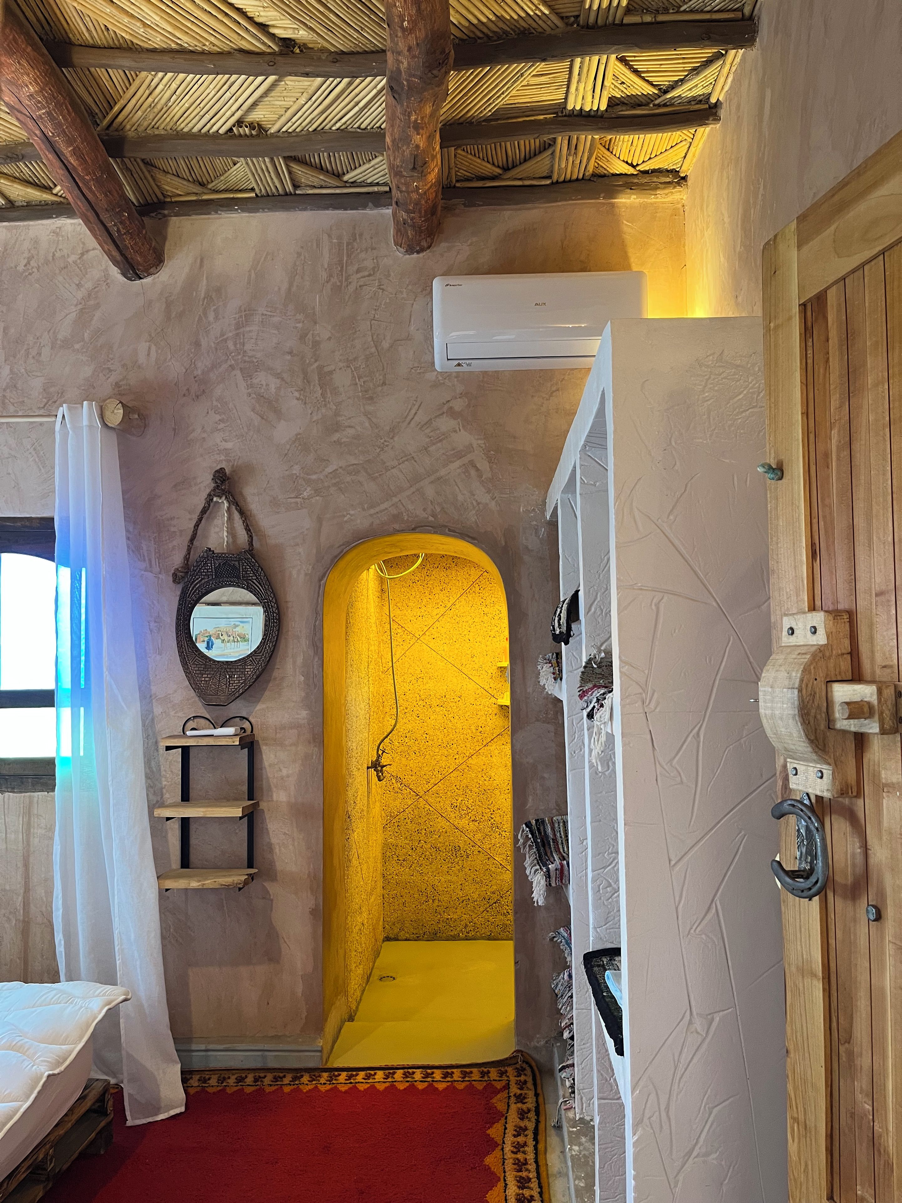A room with a wooden door, a white air conditioning unit, a red carpet, and a yellow wall.