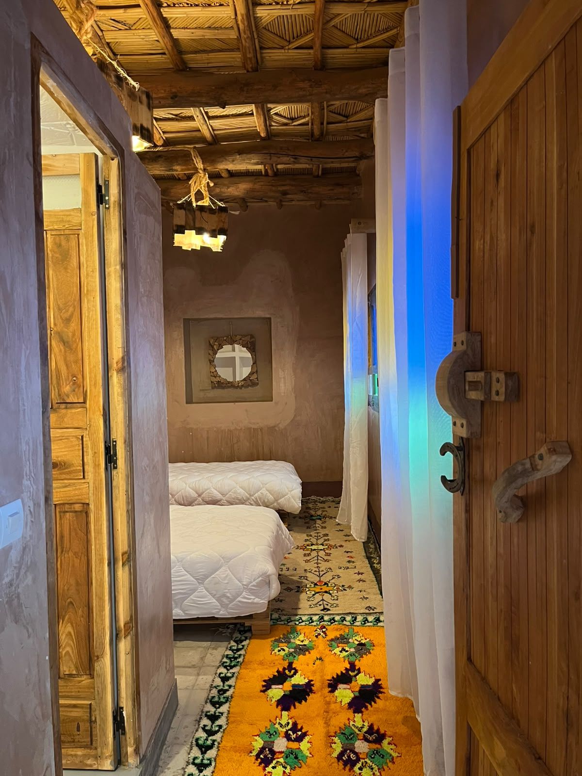 A narrow hallway with wooden doors and a patterned rug leading to a room with two beds.