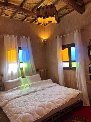 A room with a bed, curtains, a wall-mounted light fixture, and a window with a view.