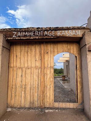 A wooden gate with the inscription 'ZAIMHERITAGE KASBAH' and an archway leading to a covered outdoor area. - Relax, Explore, and Feel at Home in the heart of Skoura Morocco (Rabat)