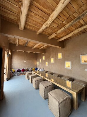 A room with a long wooden table, several cushioned stools, and a high wooden ceiling. - Relax, Explore, and Feel at Home in the heart of Skoura Morocco (Rabat)