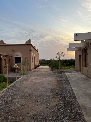 A courtyard with a gravel path, a building with a flat roof, and a small tree. - Relax, Explore, and Feel at Home in the heart of Skoura Morocco (Rabat)
