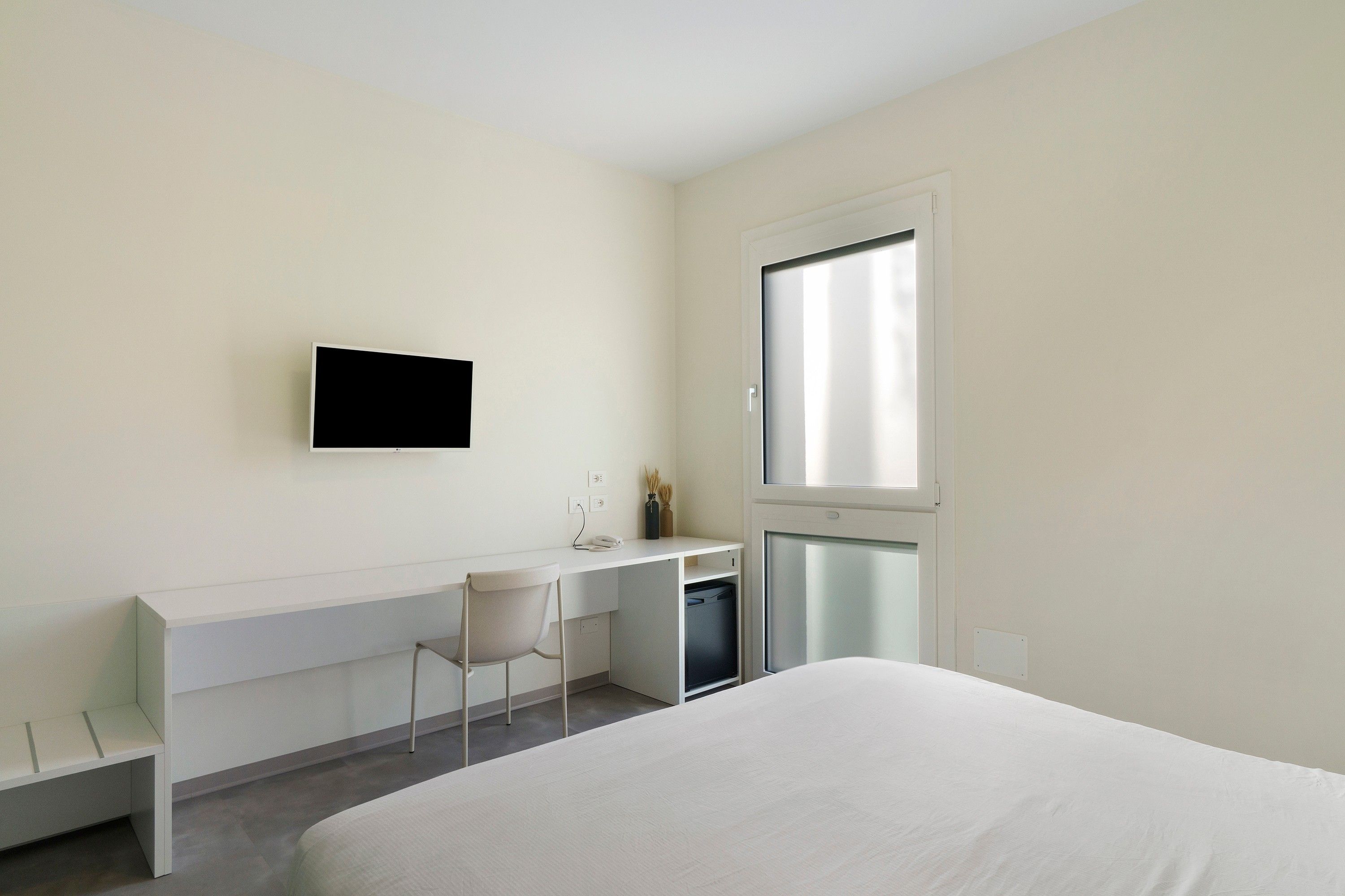 Ein Hotelzimmer mit einem Bett, einem Schreibtisch mit Stuhl, einem Fernseher und einem Fenster.