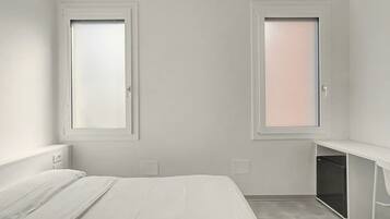 Ein schlicht eingerichtetes Schlafzimmer mit einem Bett, zwei Fenstern, einem Nachttisch und einem Einbauschrank.