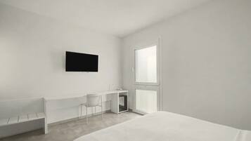 A minimalist hotel room with a bed, a desk, a chair, and a television.