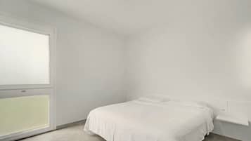 A minimalistic bedroom with a single bed, a window, and a white wall.