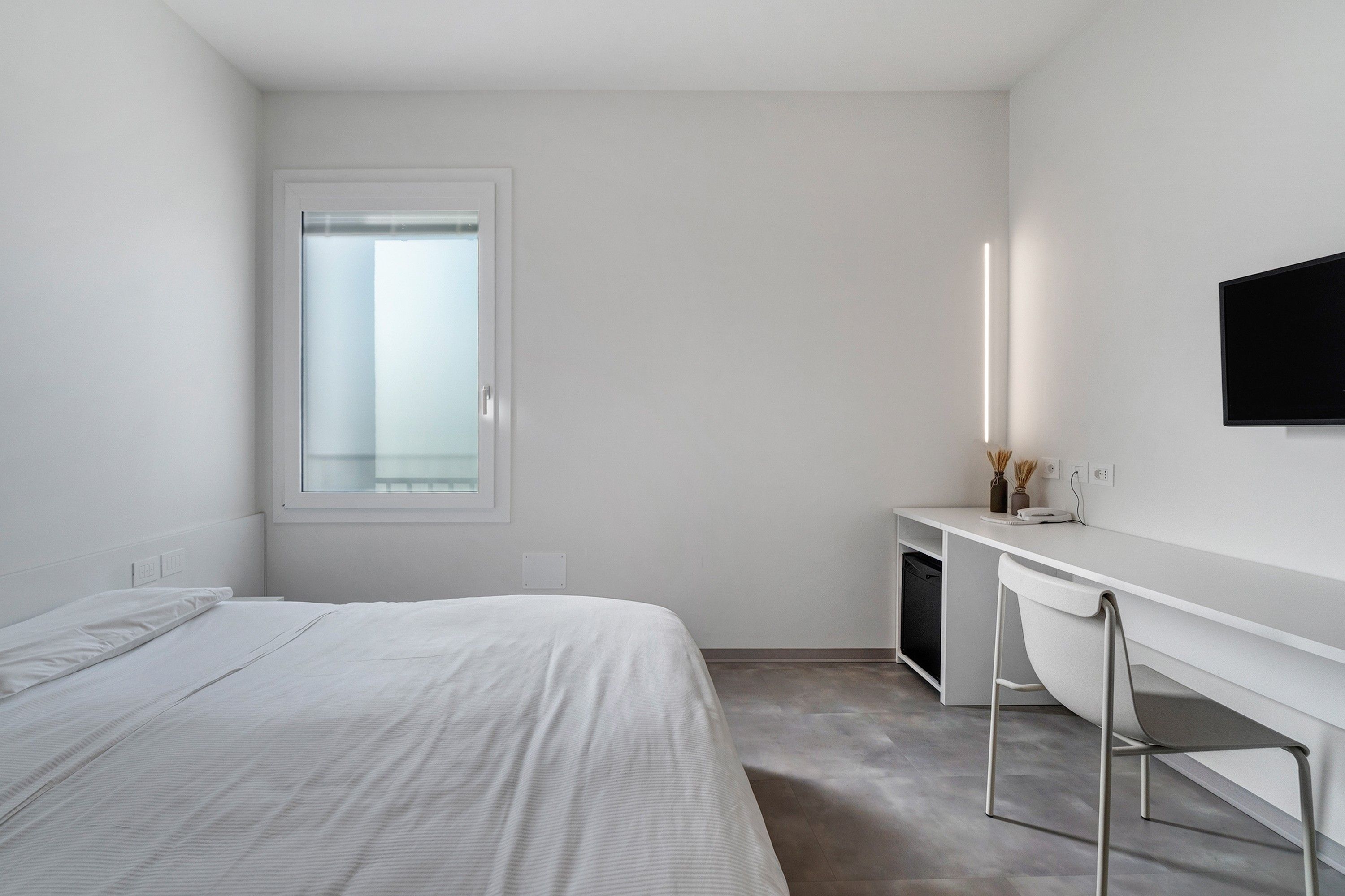 Ein schlicht eingerichtetes Hotelzimmer mit Bett, Schreibtisch, Stuhl, Fernseher und Fenster.