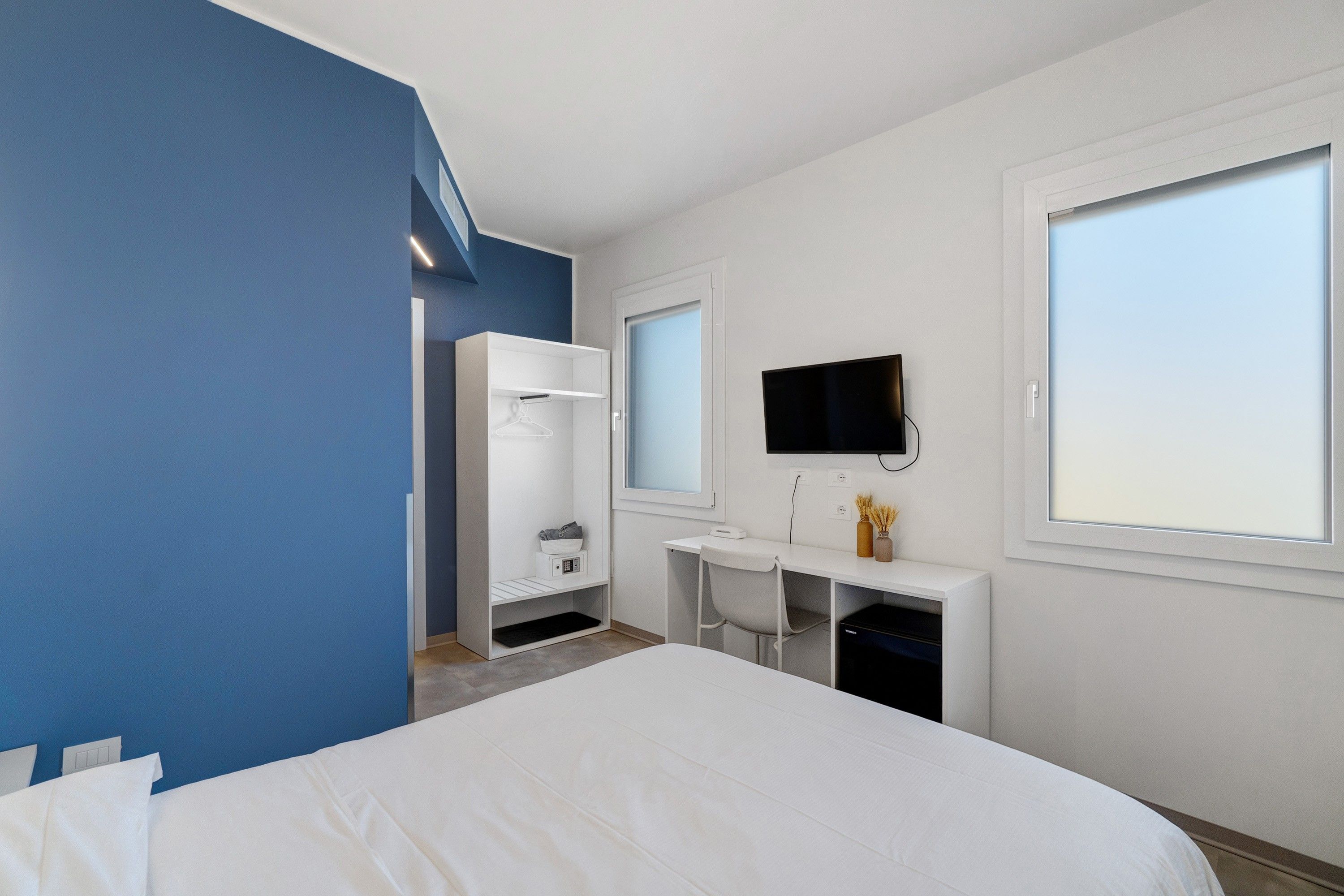 A hotel room with a bed, a desk, a TV, and a wardrobe.
