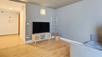 Ein Zimmer mit einem Flachbildfernseher auf einem Holzbodenständer, einer weißen Sprossenleiter und einem Korbkörbchen mit getrockneten Blumen.