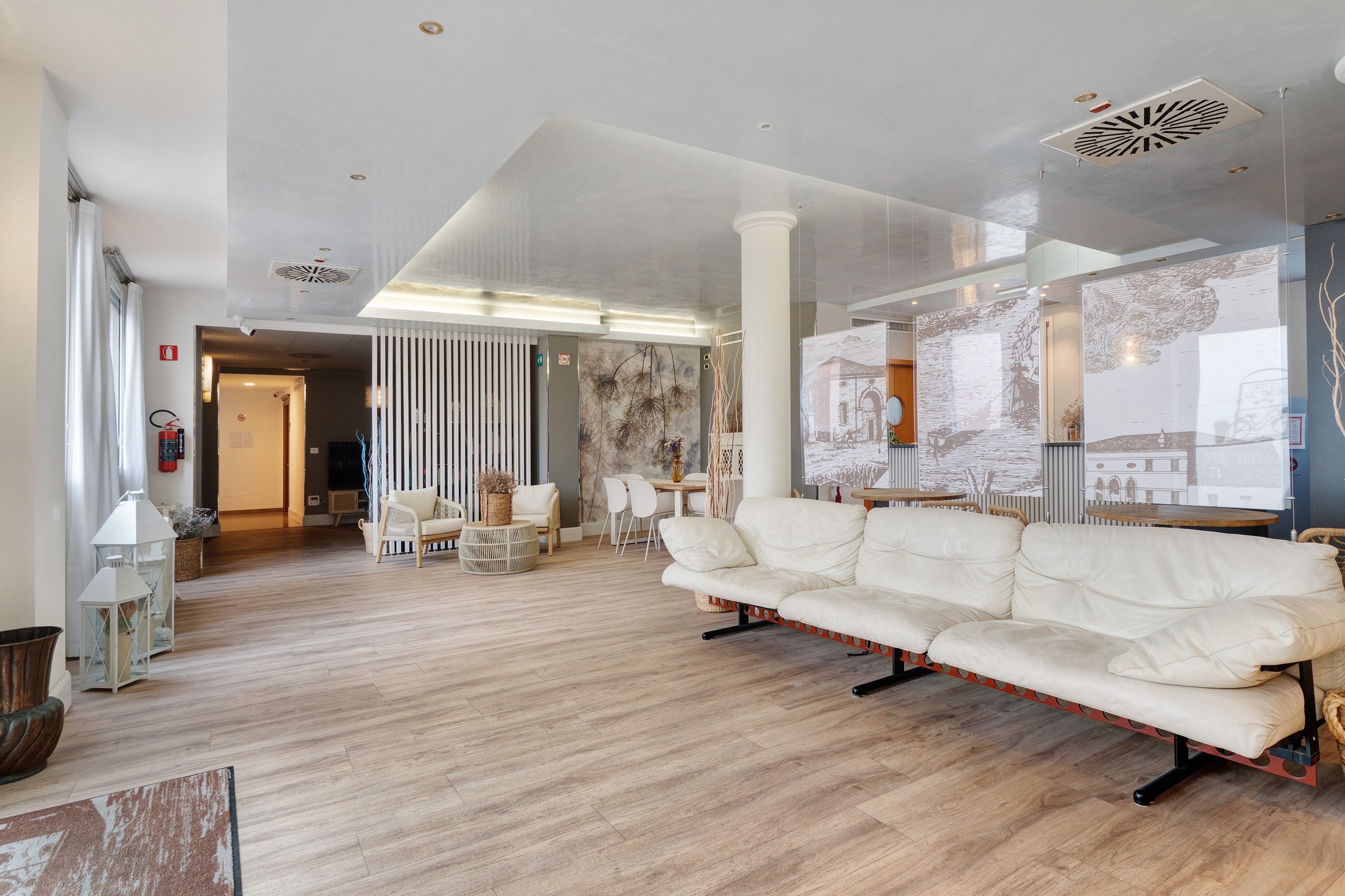 A spacious living area with a white sofa, wooden flooring, and a large window with artwork.