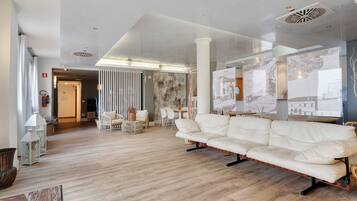 A spacious living area with a white sofa, wooden flooring, and a large window with artwork.