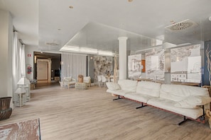 Ein geräumiges Wohnzimmer mit einem weißen Sofa, einer Essecke mit Stühlen und einem großen Wandbild.