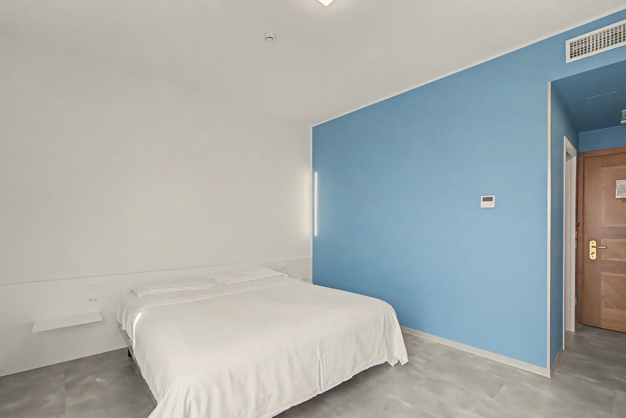 Une chambre avec un lit simple, un mur bleu et une porte en bois.