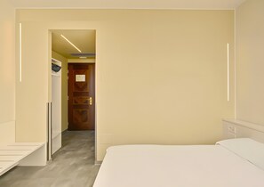 Habitación de hotel con cama, escritorio, armario y puerta que da a otra habitación.