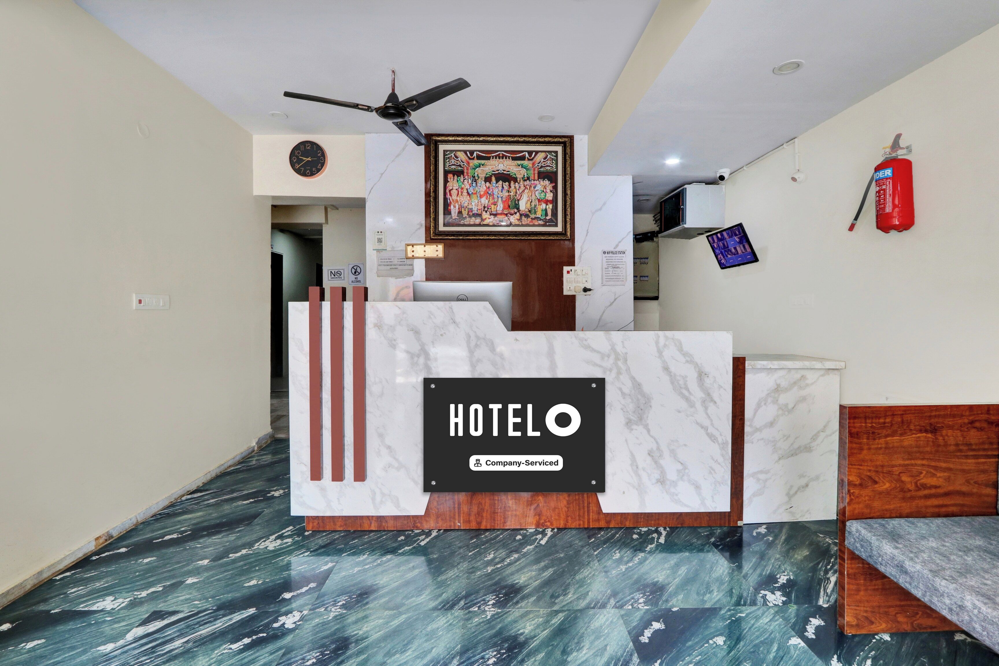 A hotel reception desk with a marble top, a ceiling fan, a framed picture on the wall, and a fire extinguisher.