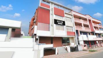 A multi-story hotel with a prominent 'HOTEL' sign, a staircase leading to the entrance, and a gated driveway.