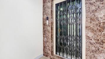 A room with a marble wall, a window with a metal grille, and a small indoor plant.
